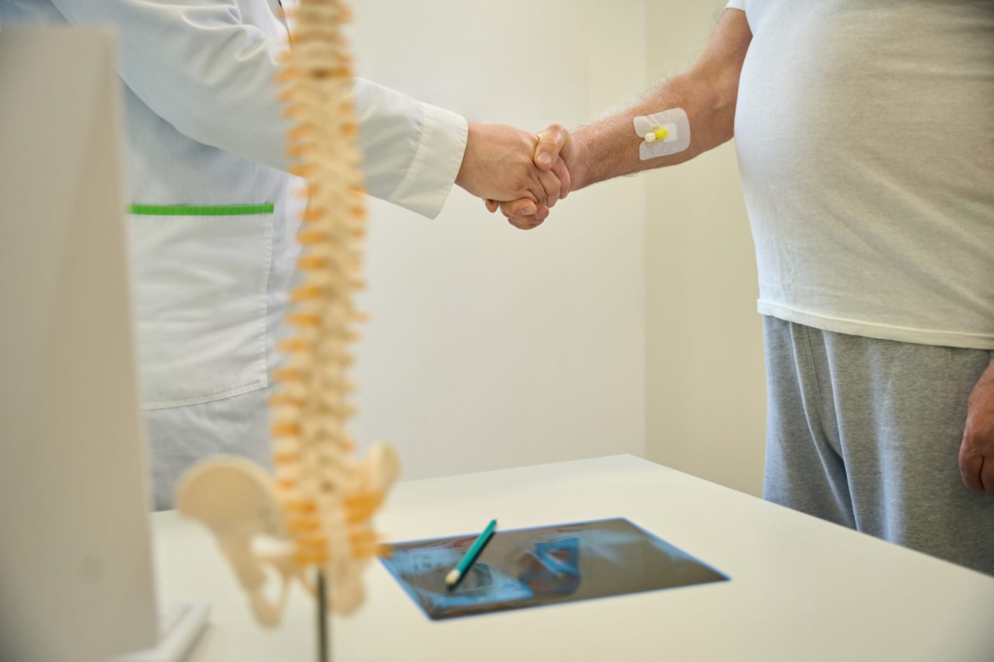 Patient and a doctor shake hands in a neurologist office while standing near the table