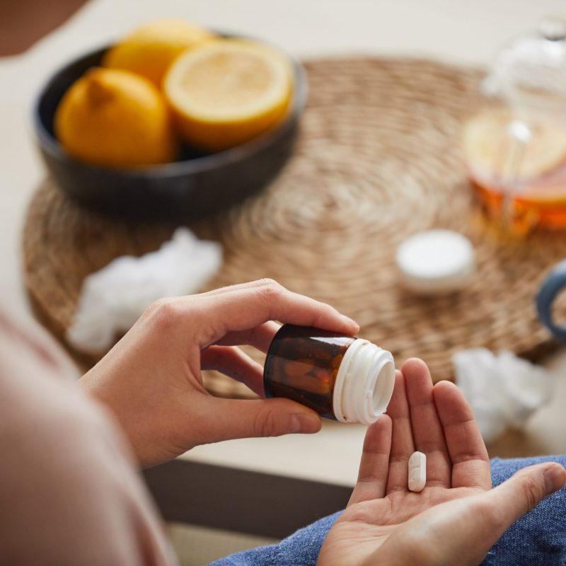 Close-up of young woman taking medicine from disease she sitting at home and treating herself